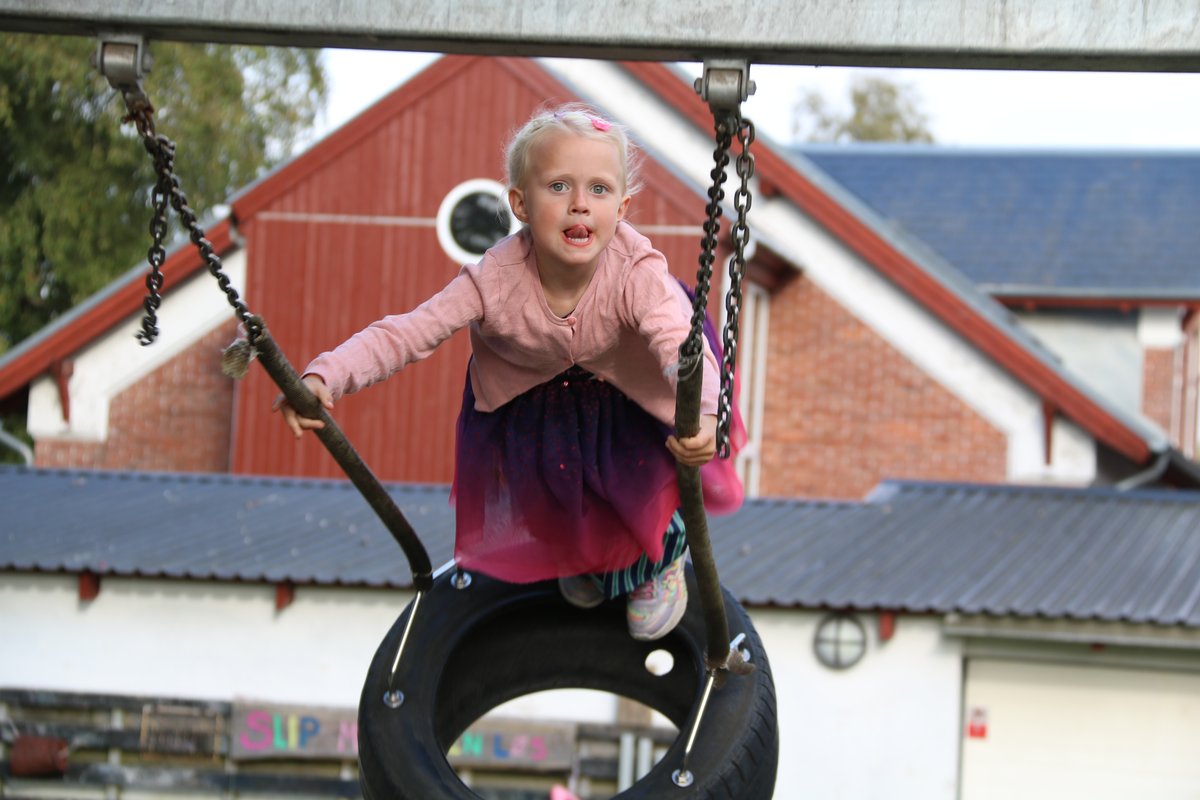Dækgynge i børnehaven Barn i dækgynge foran rød murstensbygning på børnehavelegepladsen.