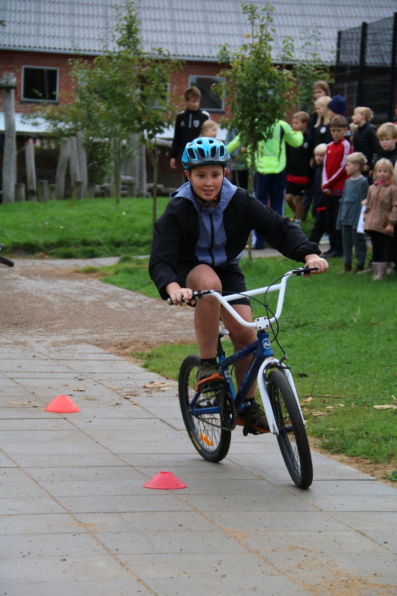 Elev på BMX mellem kegler Elev på BMX-cykel mellem orange kegler på asfalt foran skolebygningen.