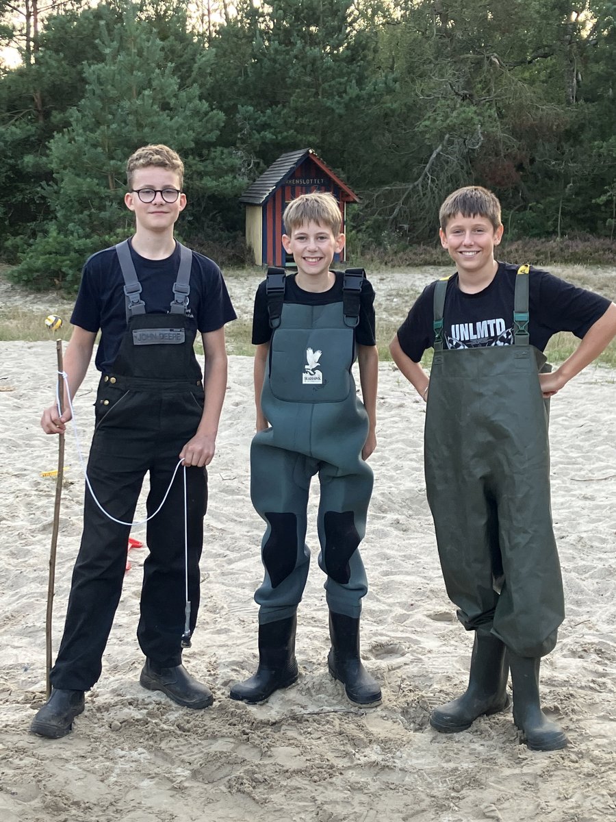 Elever i waders Tre drenge i waders står på sand foran legehuset Børneslottet.